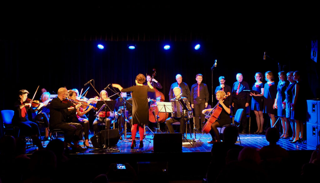 Zdjęcie pokazuje scenę na której występuje chór i orkiestra Formacji Tango Para Todos (21 osób) pod batutą Agnieszki Kowalskiej.