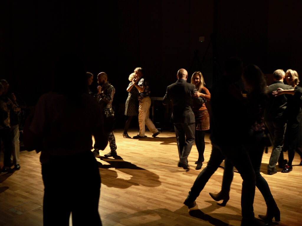 Na zdjęciu jest przygaszone światło. Widać 6 par tańczących tango.