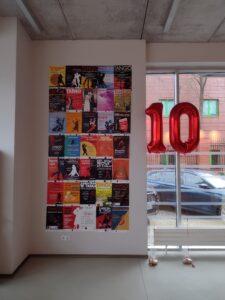Ściana plakatów koncertów Formacji Tango Para Todos. Na tle okna czerwone balony w formie dziesiątki