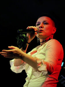 Śpiewa wokalistka Agnieszka Kowalska. W ręku trzyma mikrofon, drugą ręką gestykuluje.