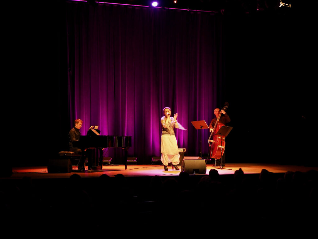 Na przyciemnionej scenie Sugar Jazz Trio- od lewej pianista, wokalistka, kontrabasista
