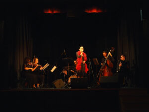 Na scenie zespół Tango Mio. Na przędzie wokalistka ubrana w szarą sukienkę z długim czerwonym boa